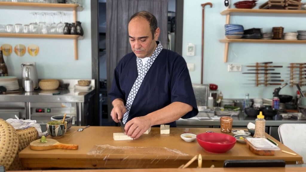 Juan preparando la ensalada de tofu sedoso. El bastón de Kikuchi, observándole al fondo